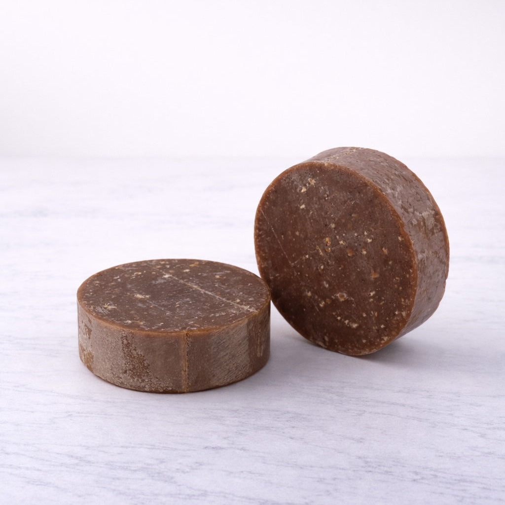 Two brown, lightly-speckled round soaps on a white background