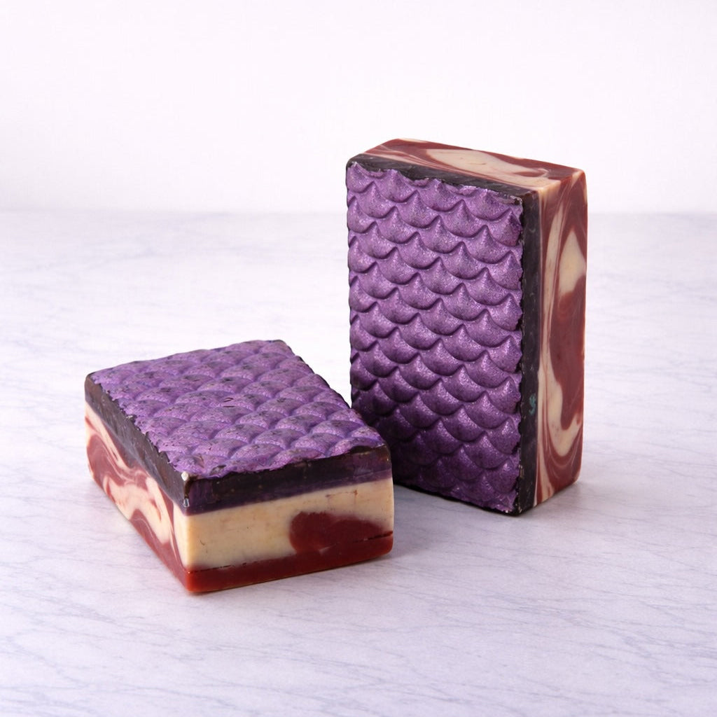 Two purple mermaid-scale patterned soap bars on a white background