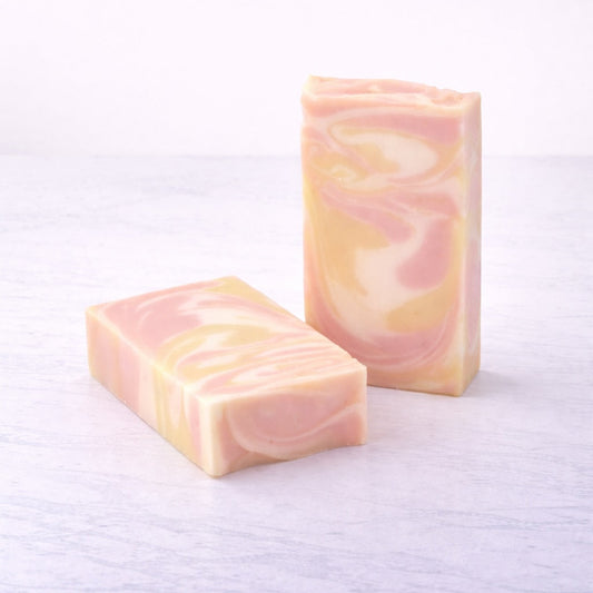 Two bars of pink and white striped soap on a textured white surface