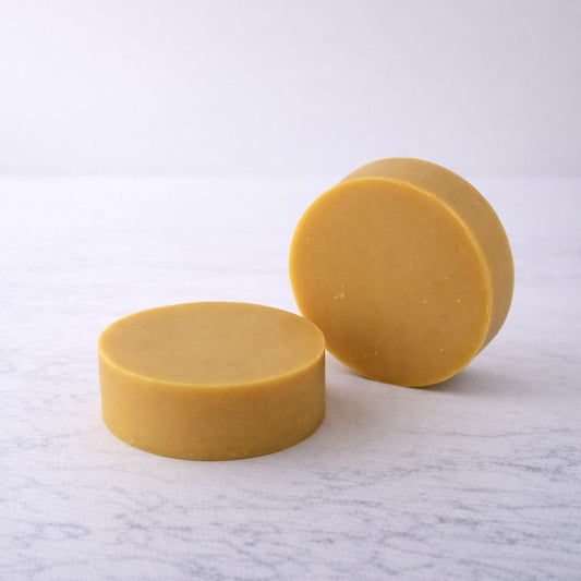Two bars of light yellow soap on a lightly textured white background