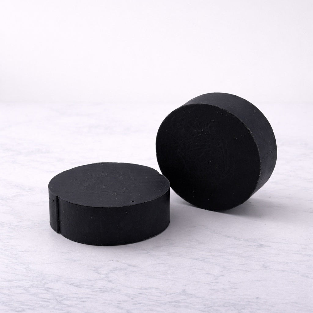 Two round black bars of soap on a light, white marble background.